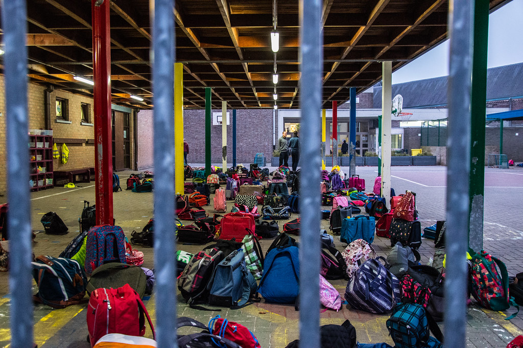 backpacks under an awning near a basketball hoop, outside a school